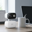 Product image of the Tapo C216 camera on a desk, next to a coffee mug for scale reference.